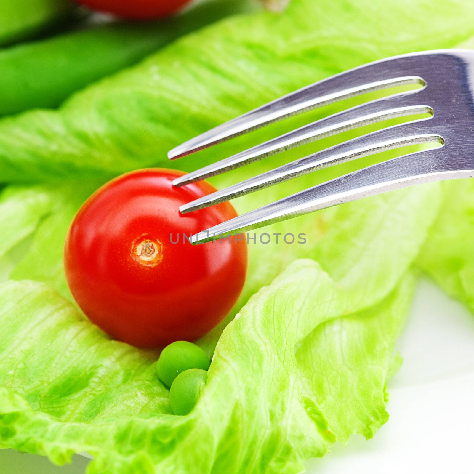 tomato,peas and lettuce with a fork on a plate isolated on white