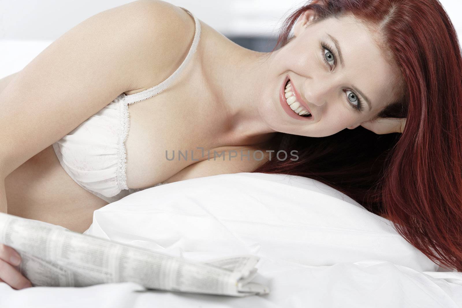 Beautiful young woman in white underwear reading a paper on her bed at home