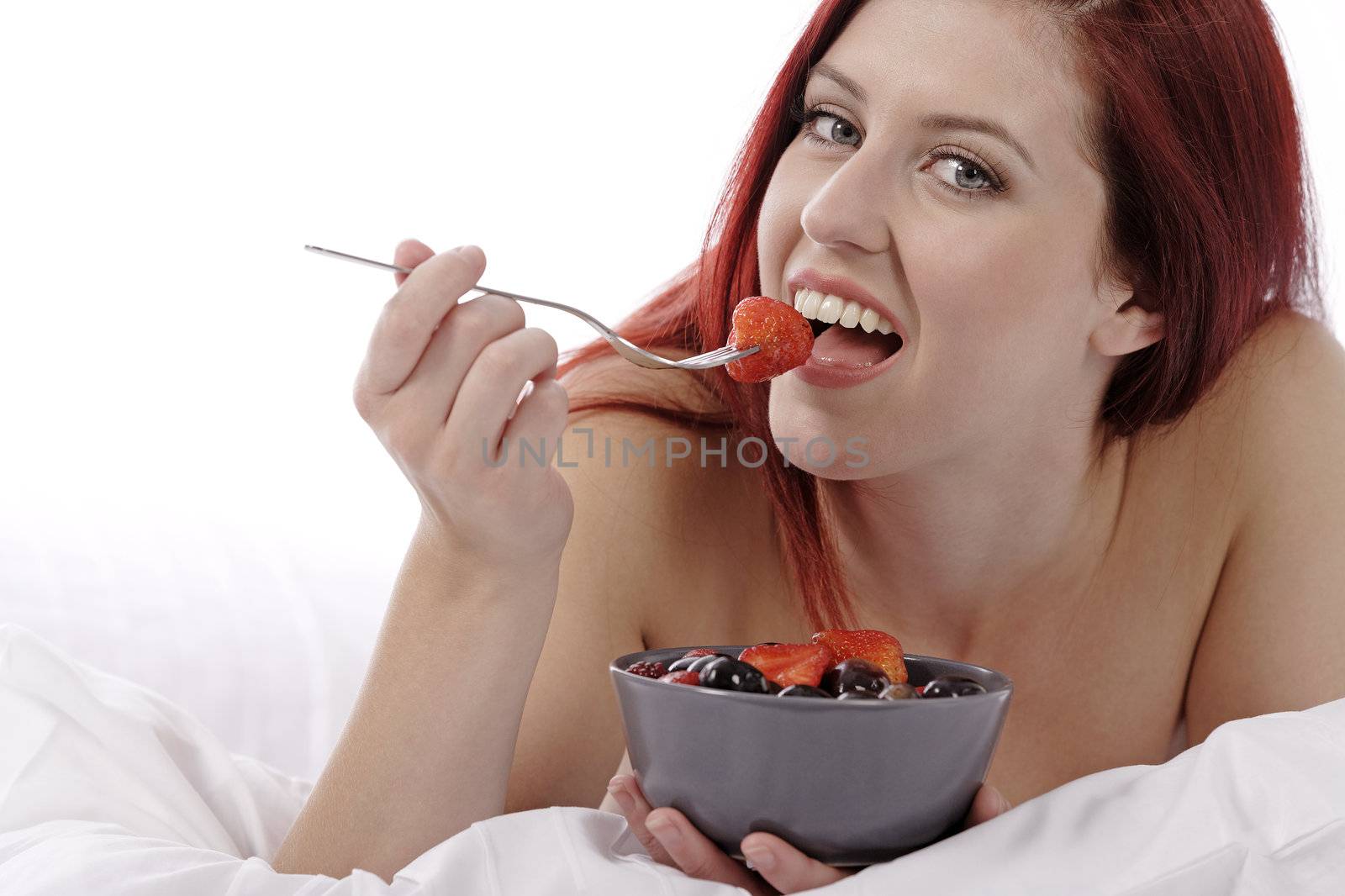 Attractive young woman on her bed at home eating fresh fruit for breakfast