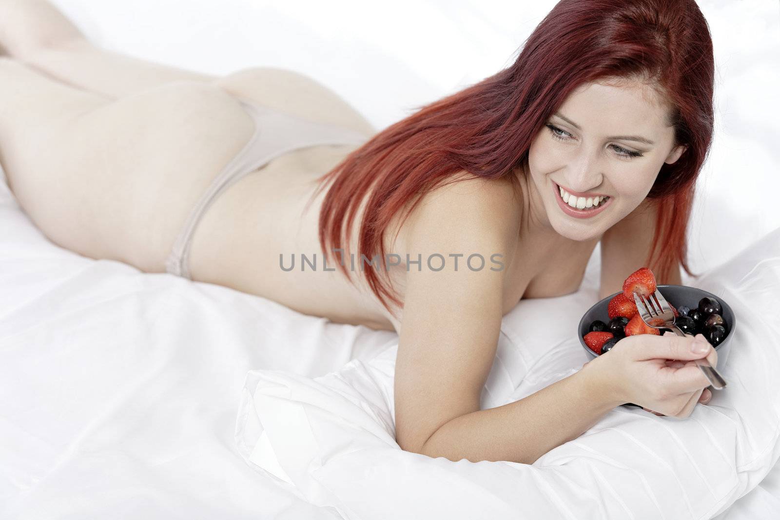 Attractive young woman on her bed at home eating fresh fruit for breakfast