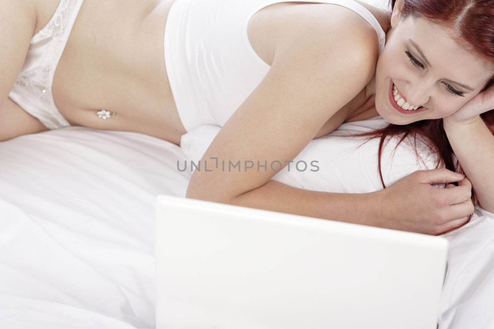 Beautiful young woman using her laptop computer on her bed, while relaxing in her underwear.