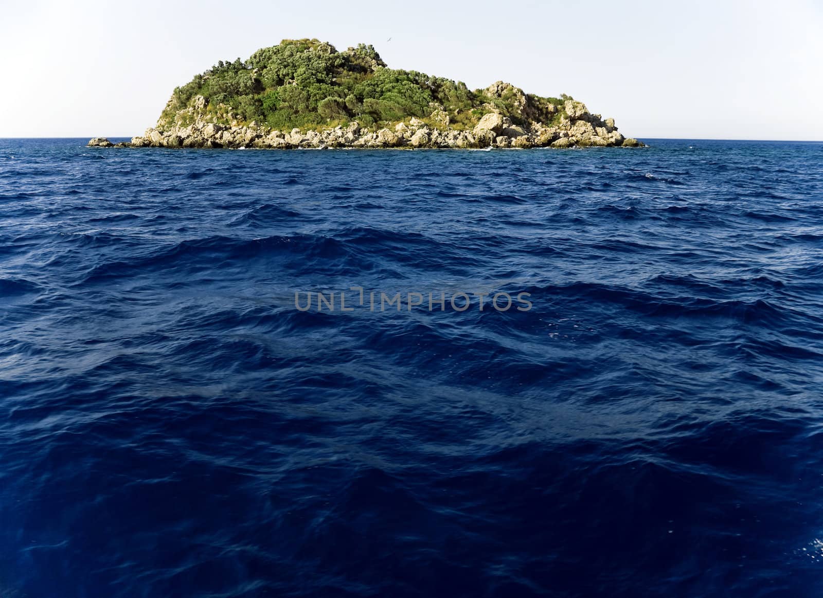 green island in the middle of the ocean waves on blue sky background
