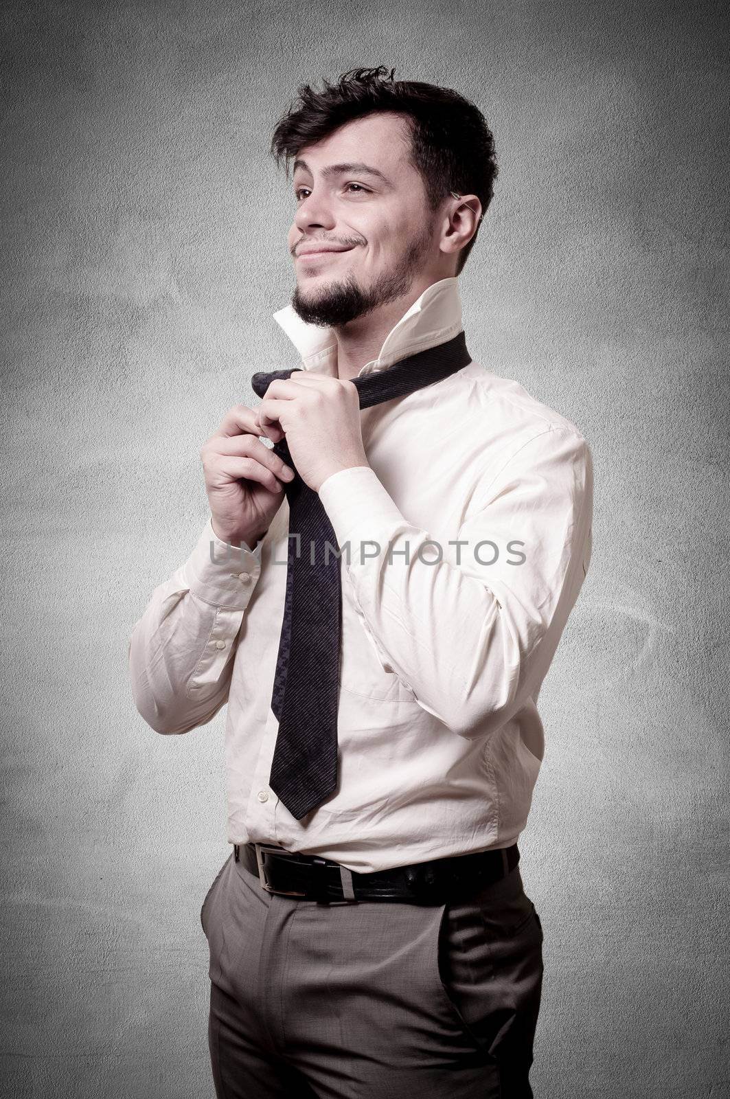 Sexy stylish businessman adjusting tie on gray background