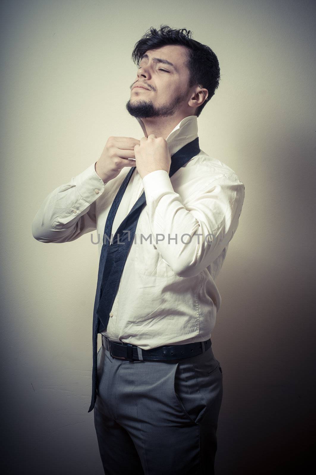 Sexy stylish businessman adjusting tie on gray background