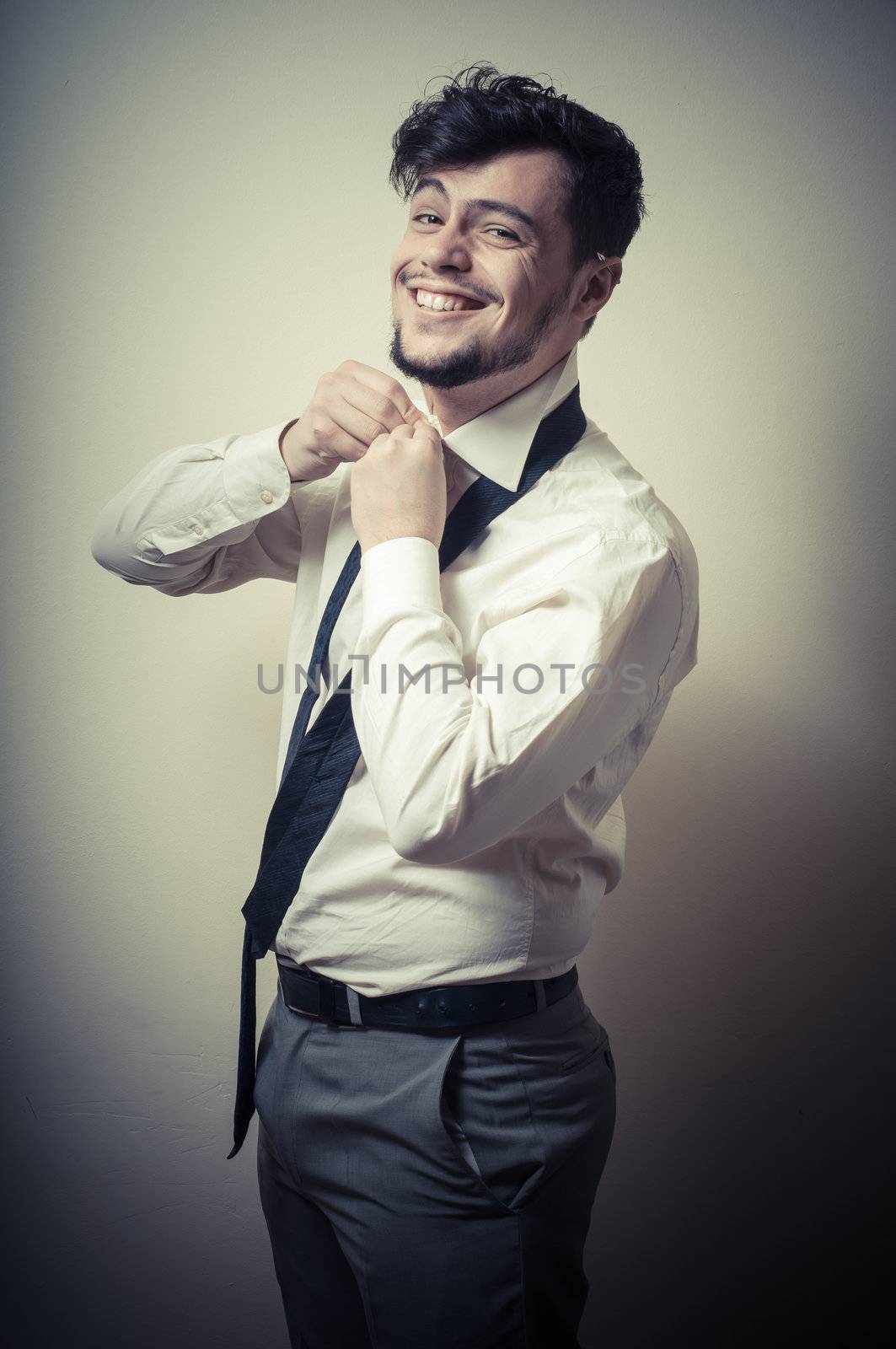 Sexy stylish businessman adjusting tie on gray background