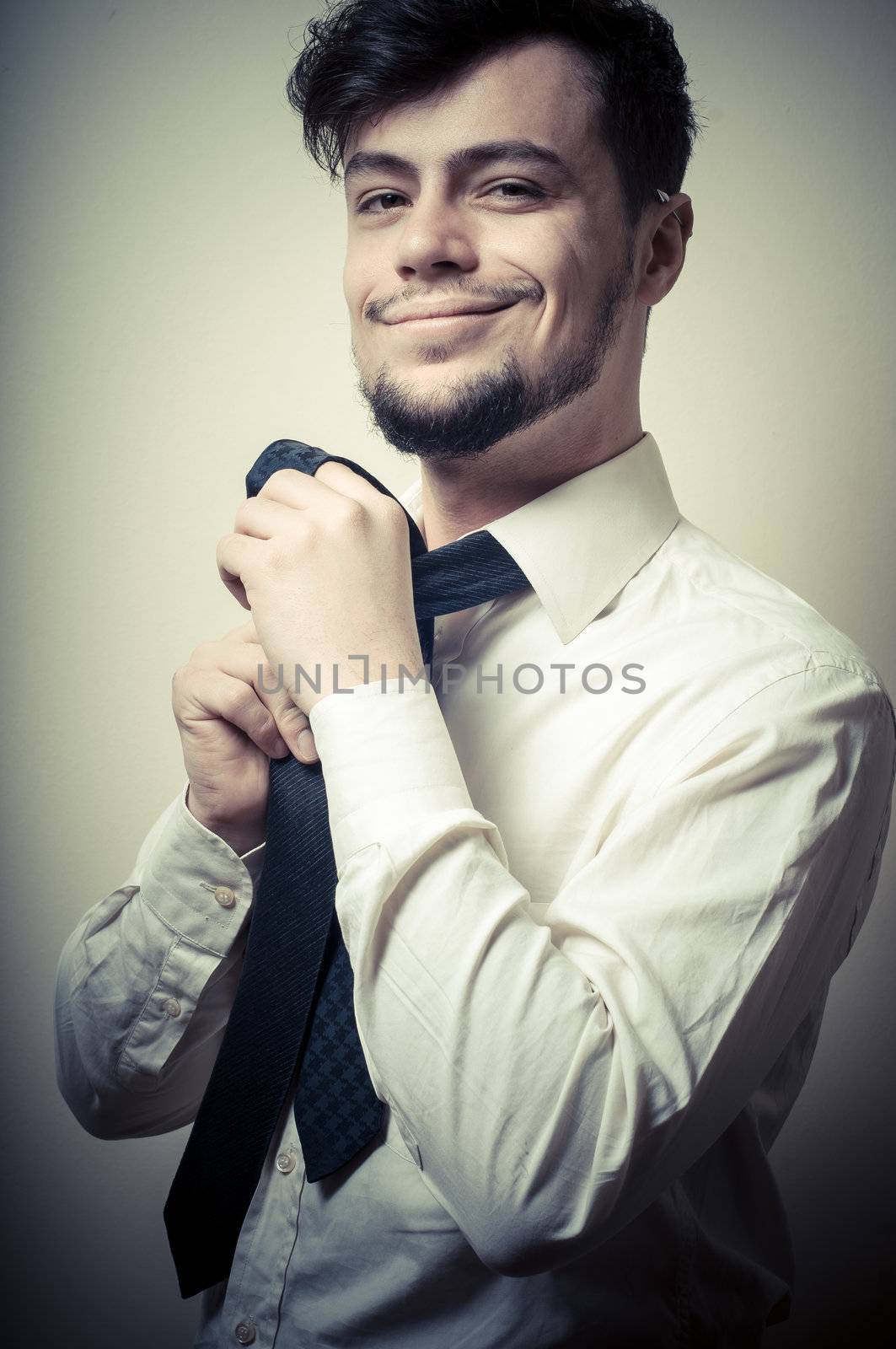 Sexy stylish businessman adjusting tie on gray background