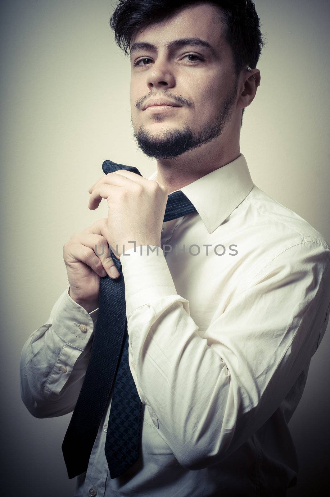 Sexy stylish businessman adjusting tie on gray background