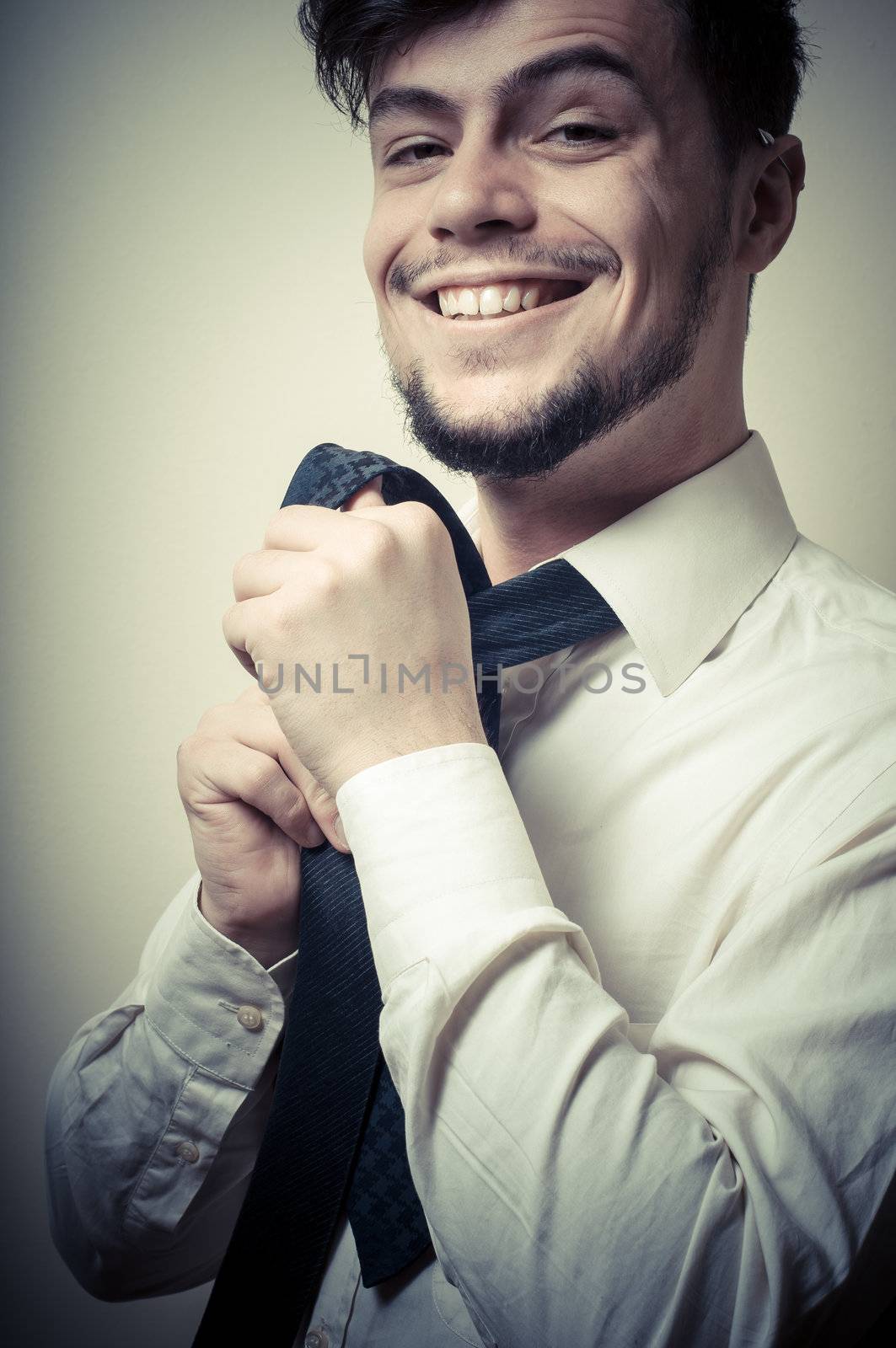 Sexy stylish businessman adjusting tie on gray background