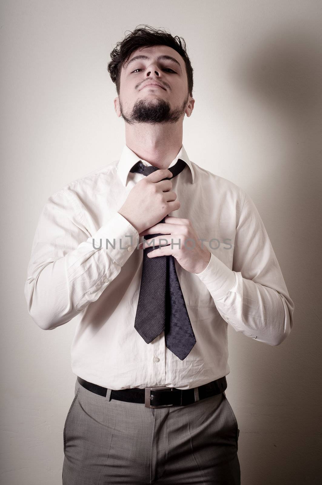 Sexy stylish businessman adjusting tie on gray background