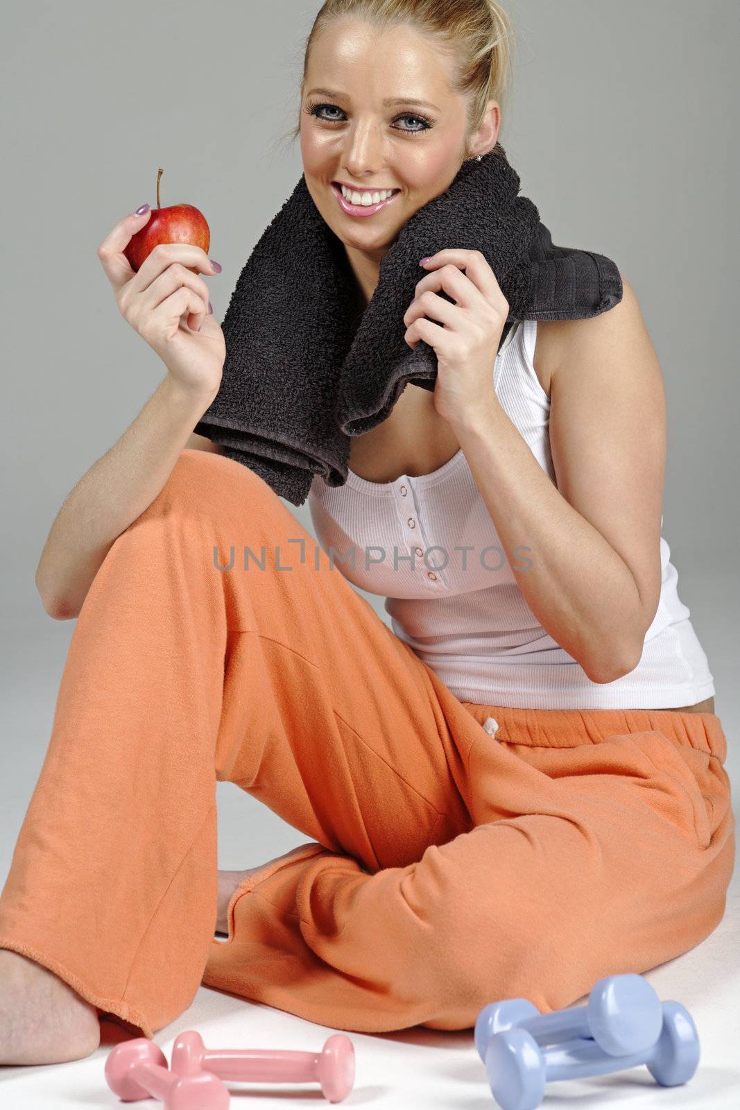 Beautiful young woman resting after exercise in fitness wear holding an apple