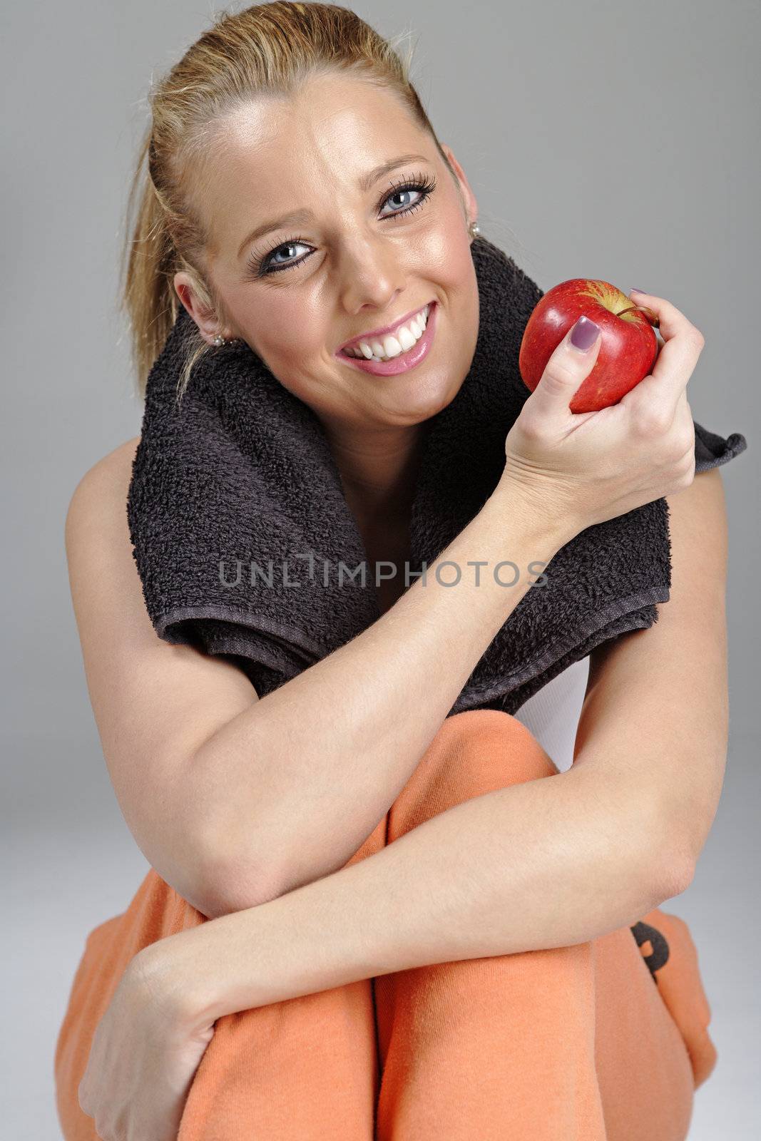 Beautiful young woman resting after exercise in fitness wear holding an apple