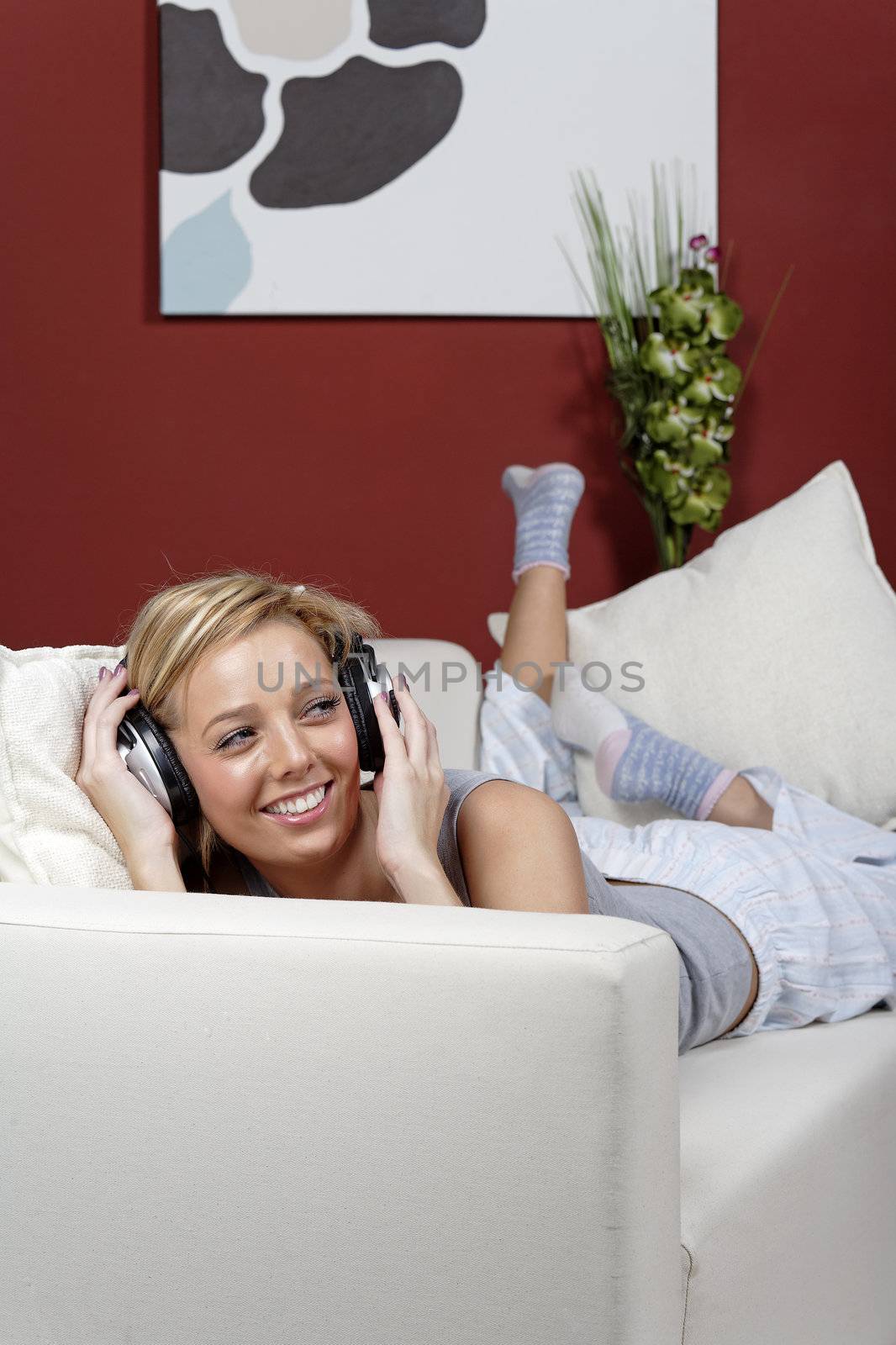 Beautiful young woman lying on sofa at home listening to music on headphones