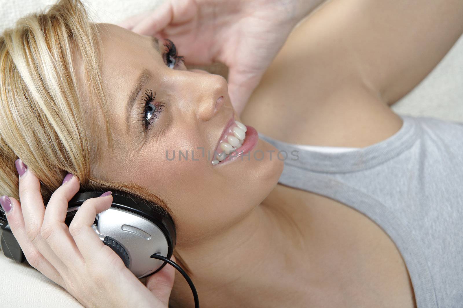 Beautiful young woman lying on sofa at home listening to music on headphones