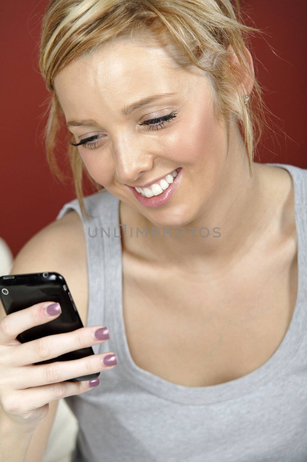 Beautiful young woman lying on sofa at home reading a text message.