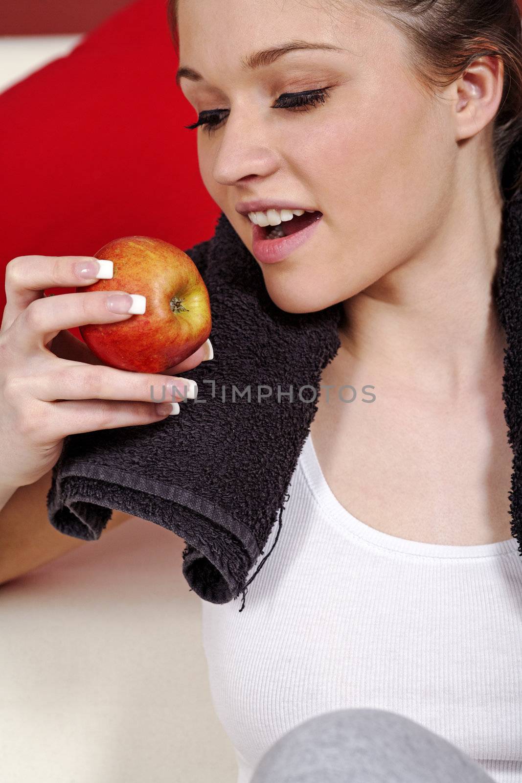 Young woman resting at home after exercise in fitness wear eating an apple