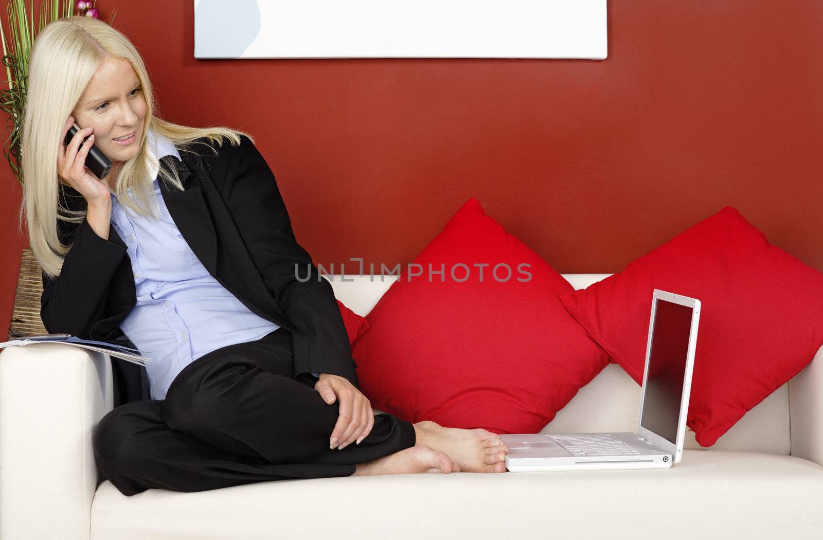 Young woman sitting on a sofa chatting on the phone and working