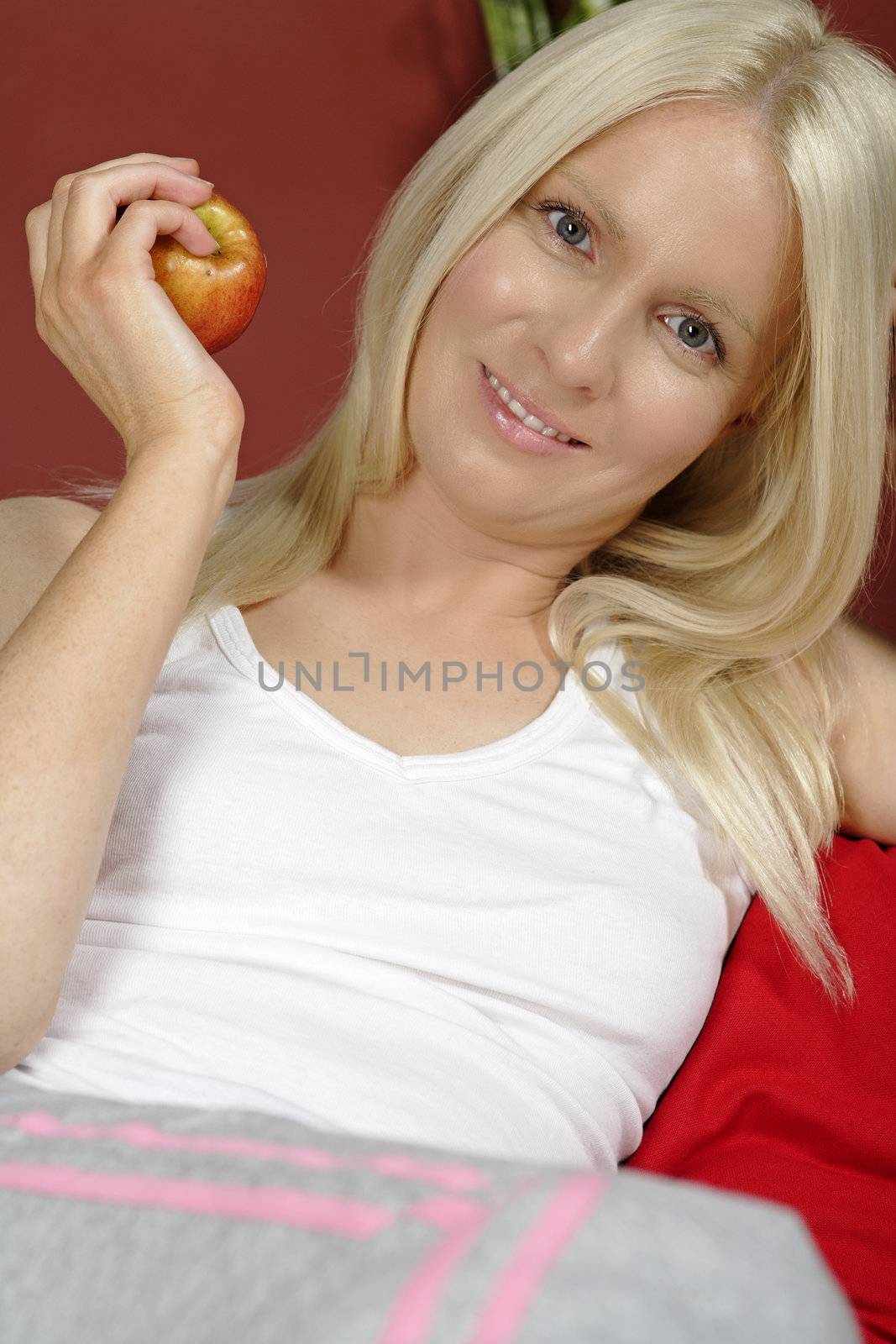 Young woman sat on sofa at home holding an apple