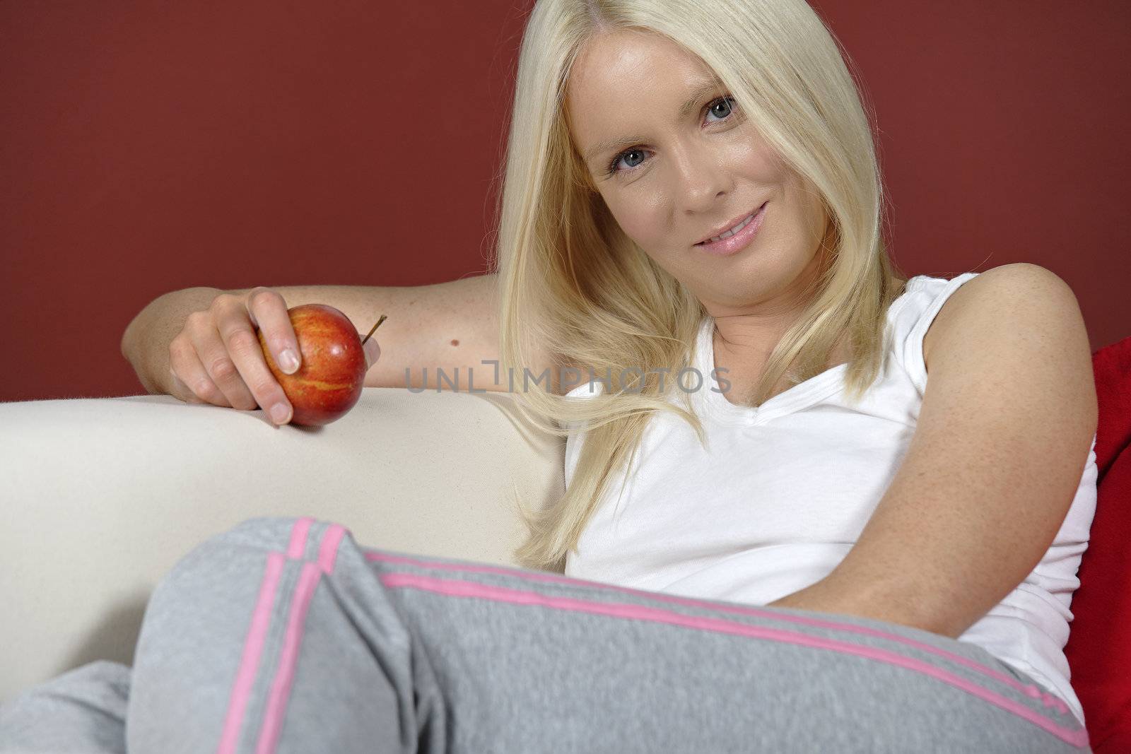 Young woman sat on sofa at home holding an apple