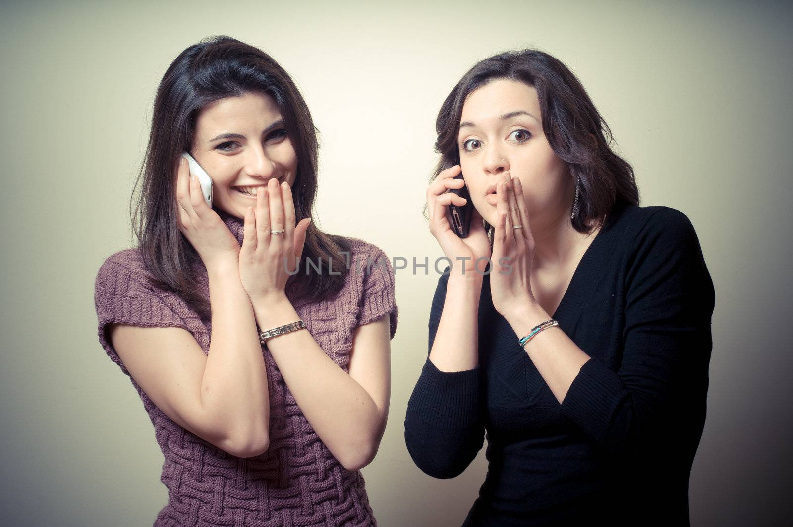 two beautiful girls gossiping on the phone on gray background