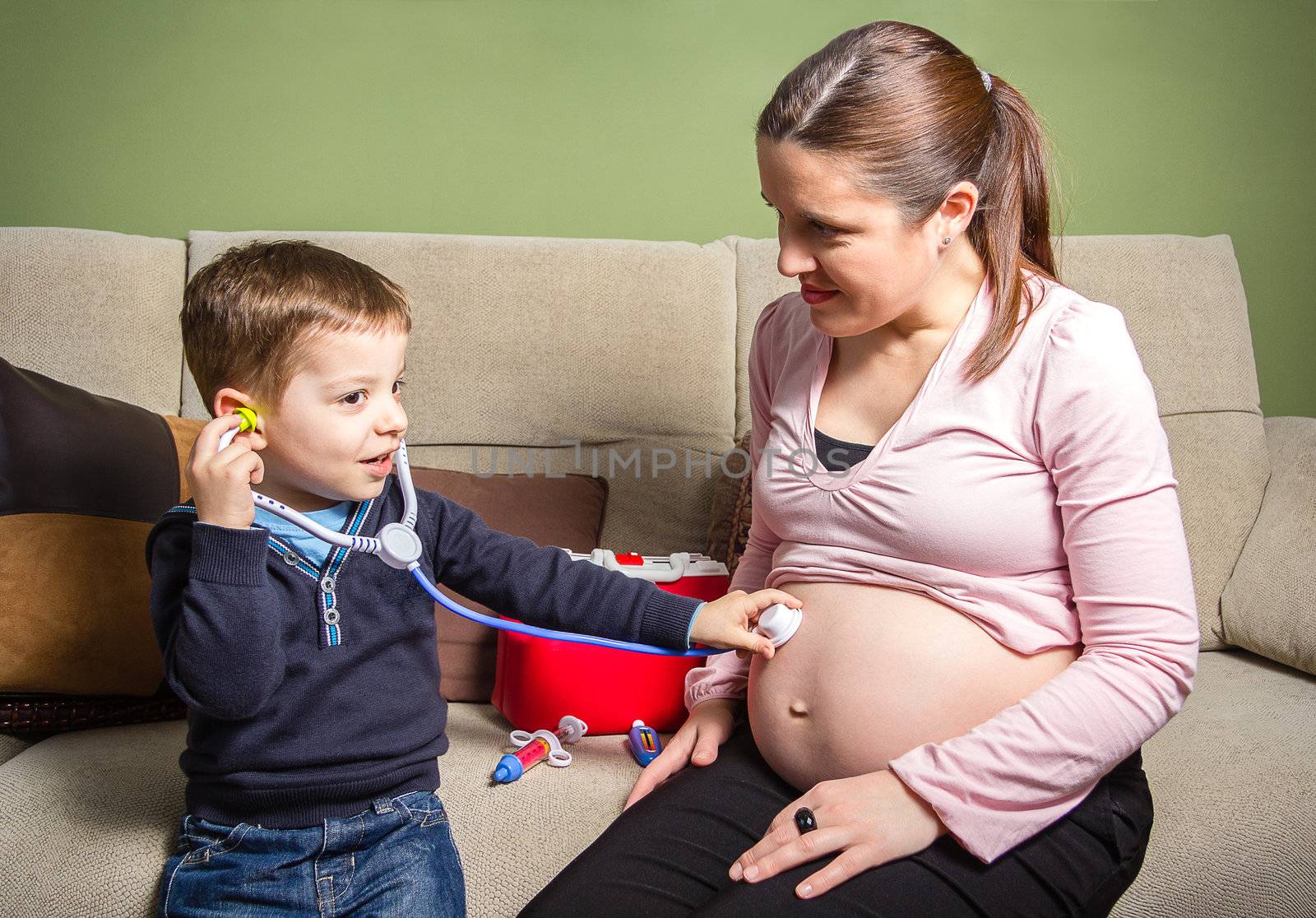 Funny child doctor examining his pregnant mother with medical toys