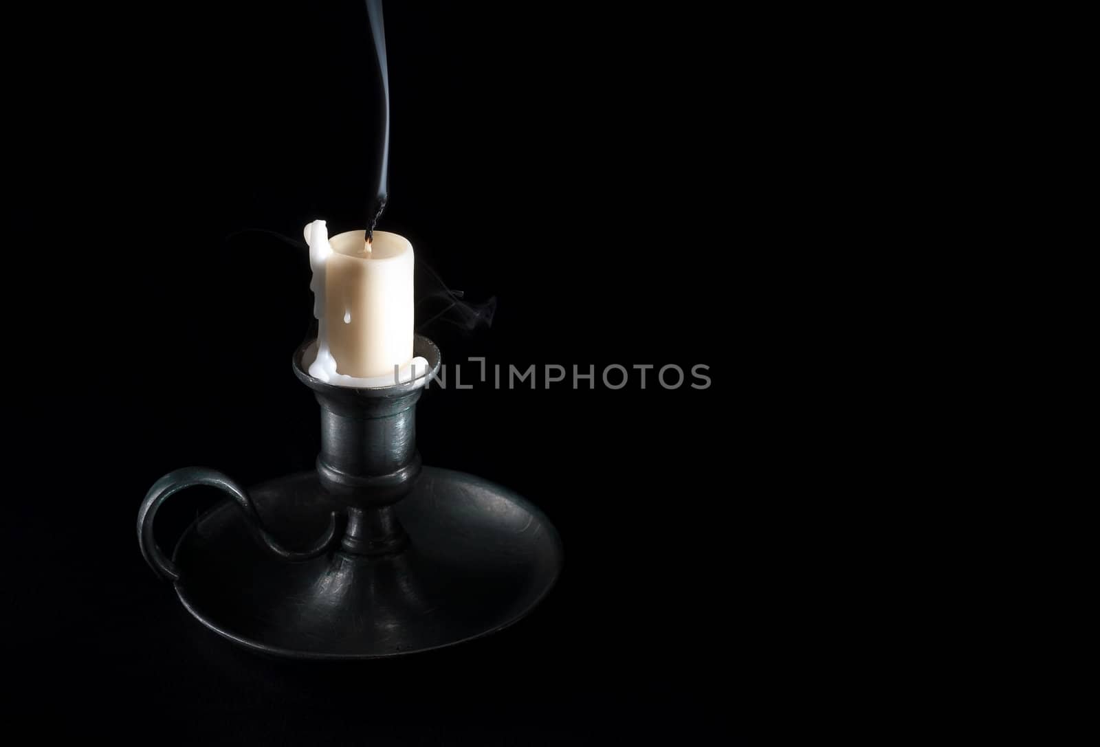 extinguished candle in an old tin candlestick and smoke on a black background