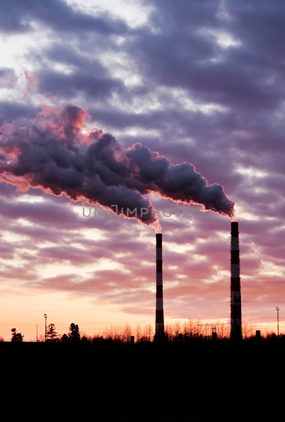 Pollution spewing into the air from industrial chimneys, at sunset.