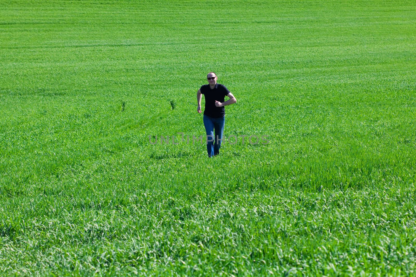 young man in sunglasses running in green field