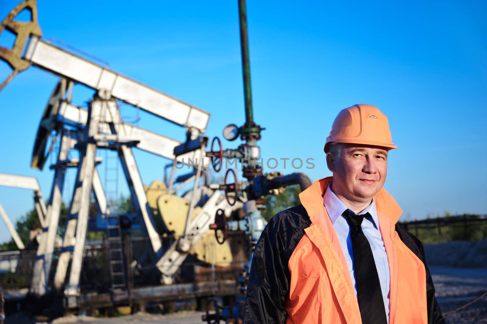 Oil worker in orange uniform and helmet on of background the pump jack and blue sky.