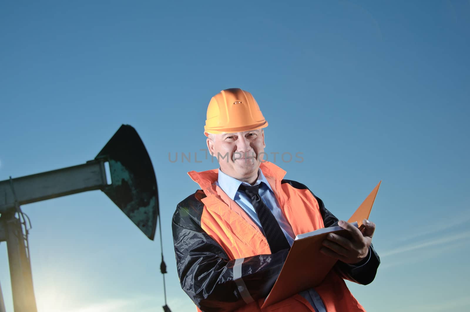 Oil worker in orange uniform and helmet on of background the pump jack and blue sky.