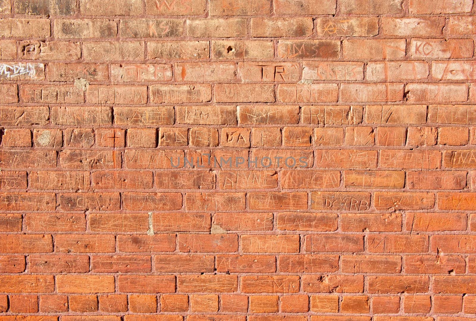 An old, red brick wall that has had many names carved into it.