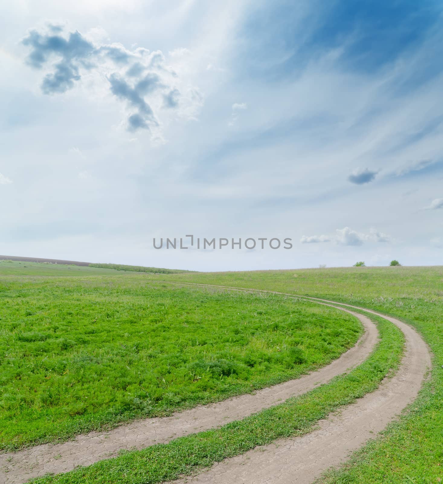 green field with dirty road under cloudy sky