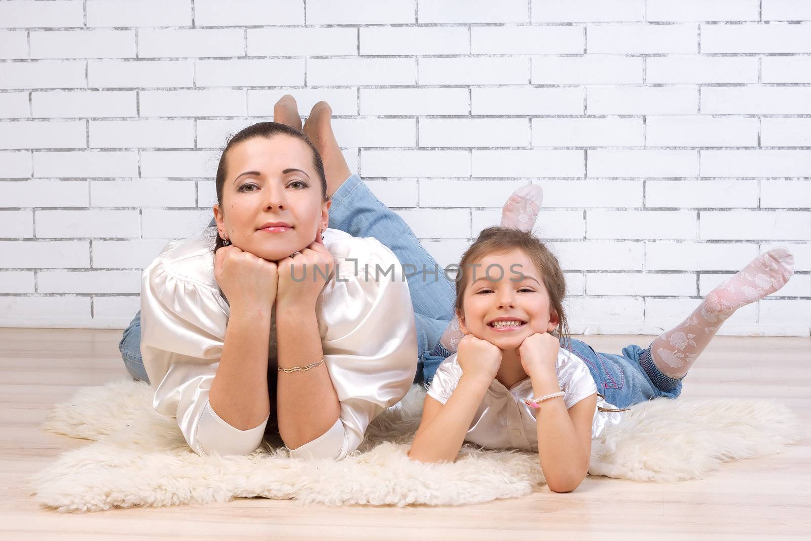 Mom with 5 year old daughter in a similar dress lying on the floor near the brick wall