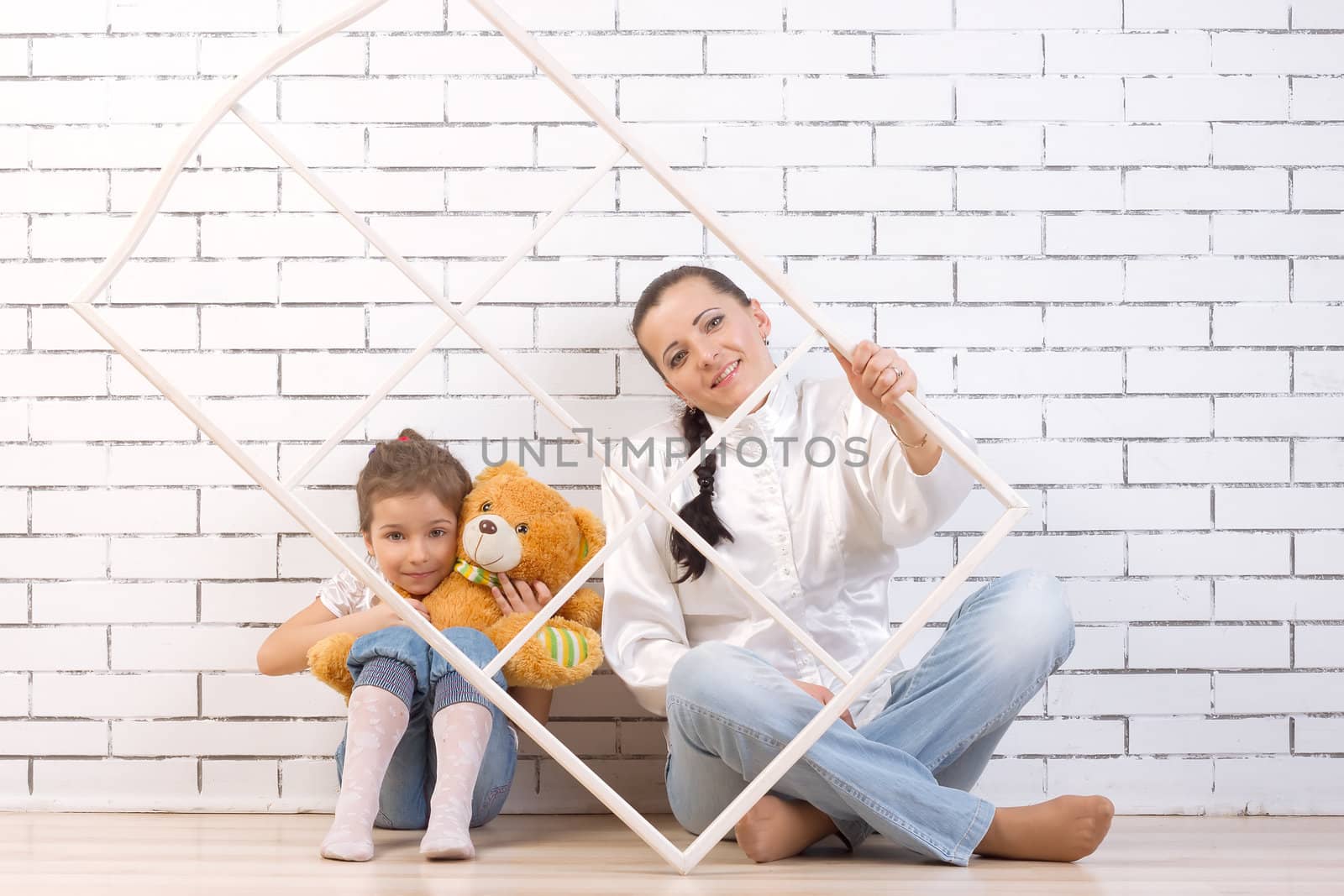 Mother and 5 year old daughter sitting by the wall, holding a toy and frame