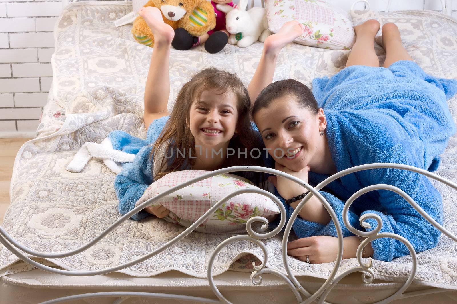 Mom and daughter in the same blue terry robes lay down on the bed