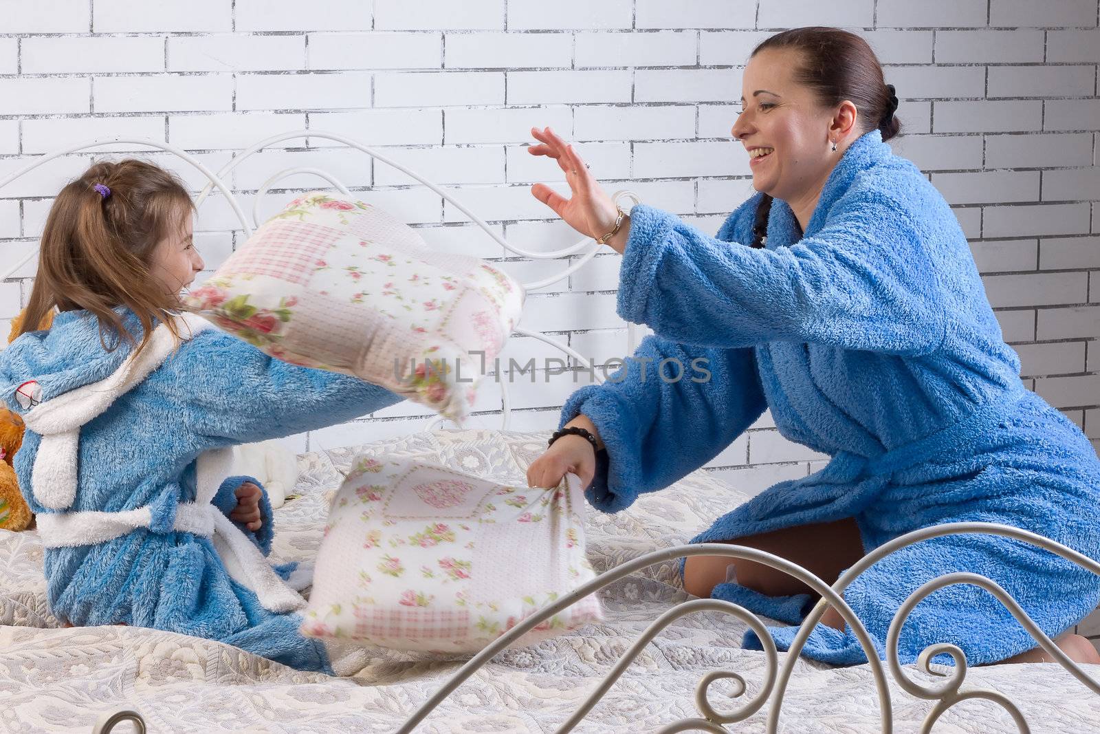 Mom and daughter in the same terry robes beat pillows