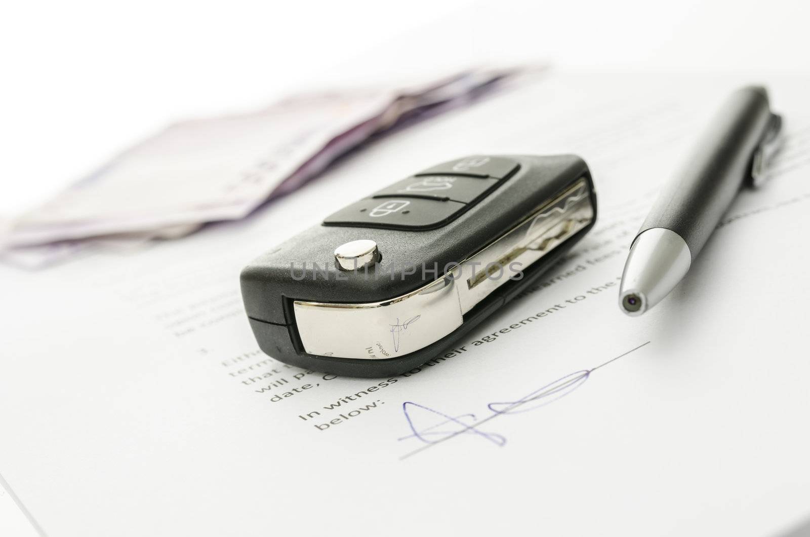 Black car key and money on a signed contract of car sale.  Focus on a key.