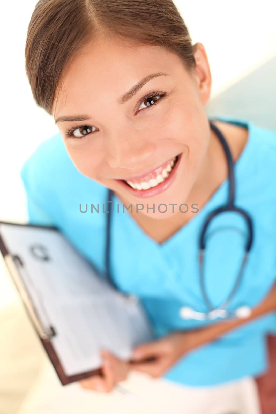Nurse medical professional young doctor closeup portrait. Young multicultural female doctor wearing blue scrubs and stethoscope in high angle perspective view. Mixed race Asian Caucasian model.