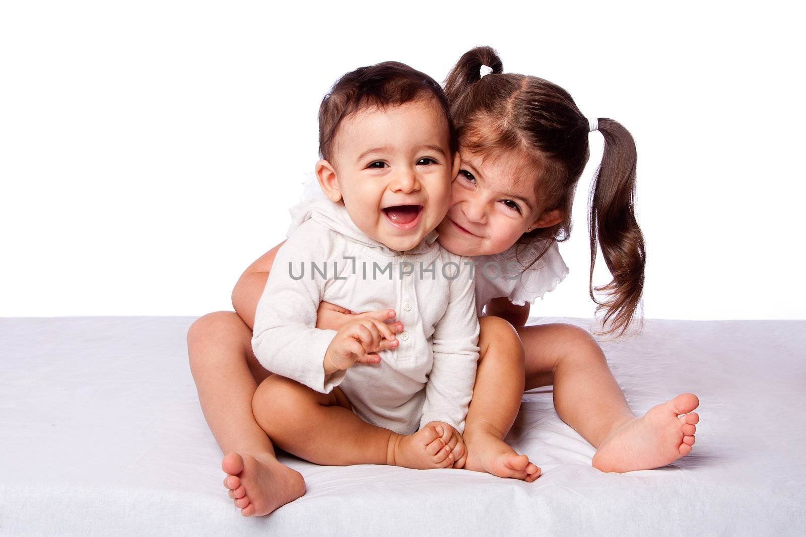 Cute lovely toddler sister hugging happy baby brother while sitting, family concept, on white.