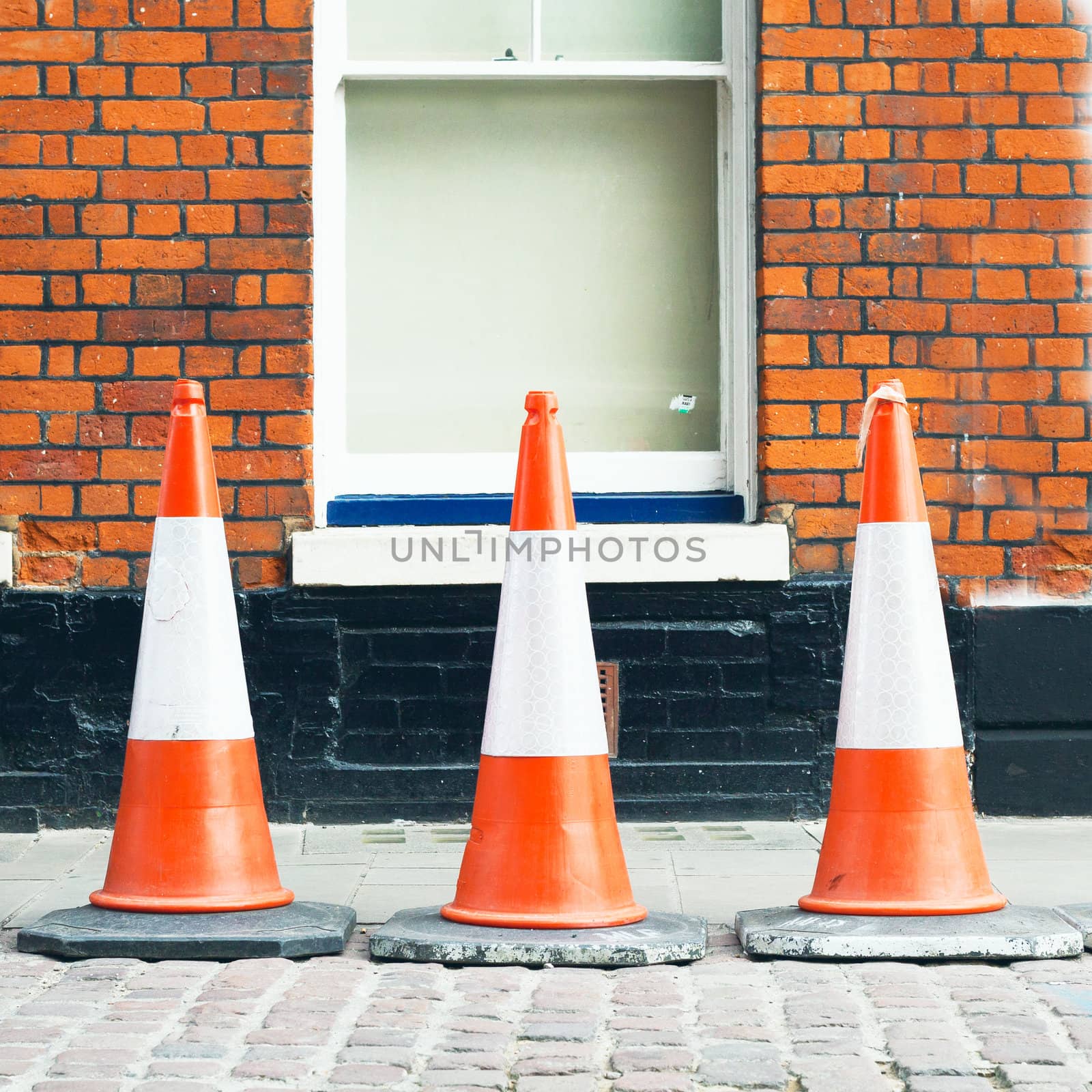 Three traffic cones in front of a brick wall