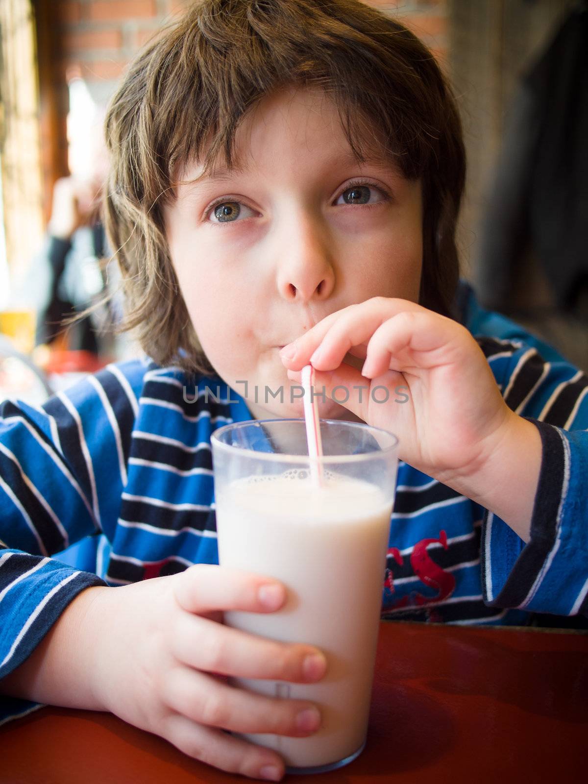 Young boy drinking a glass of milk with a straw in a restaurant