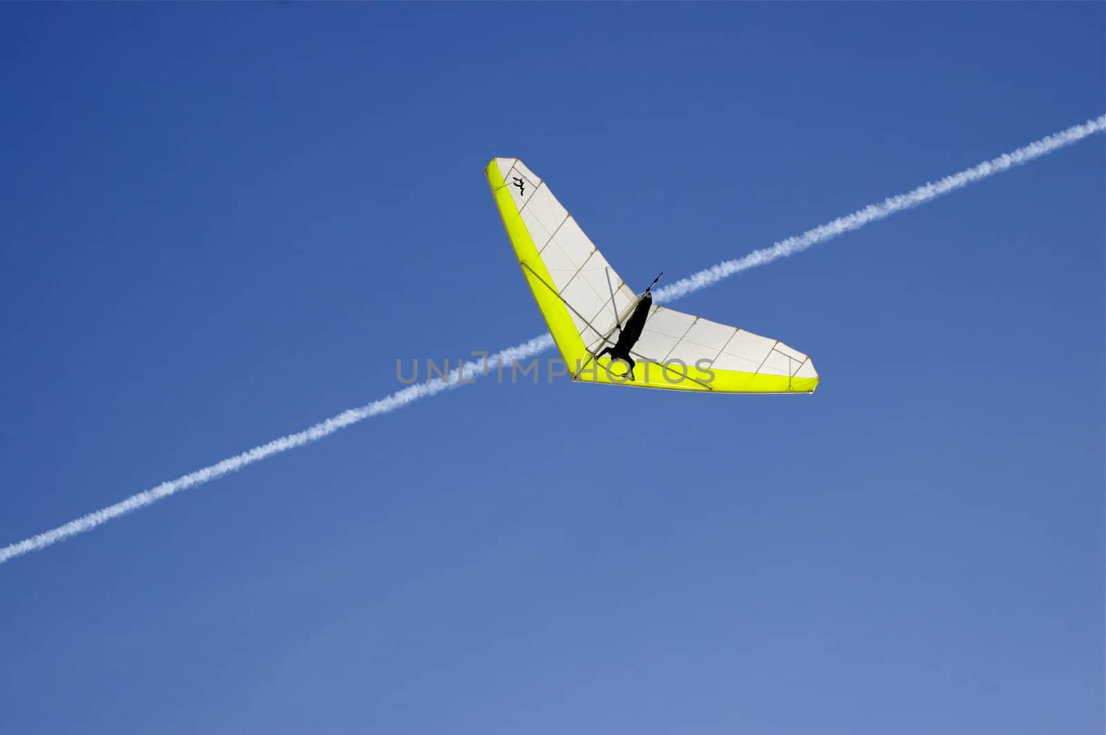 Hang Glider centre against deep blue sky with a white vapour trail criss-crossing image, with copy space.