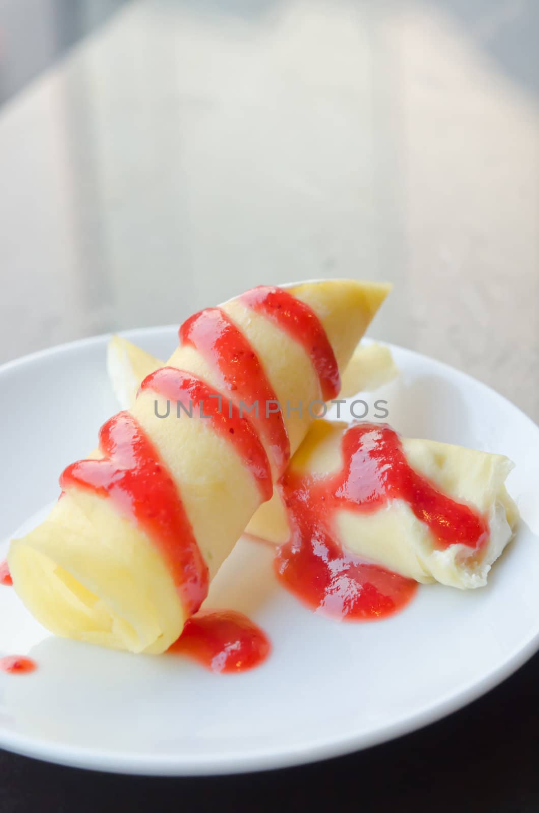 crepe rolls filled  with white cream , topping with strawberry  syrup on white dish