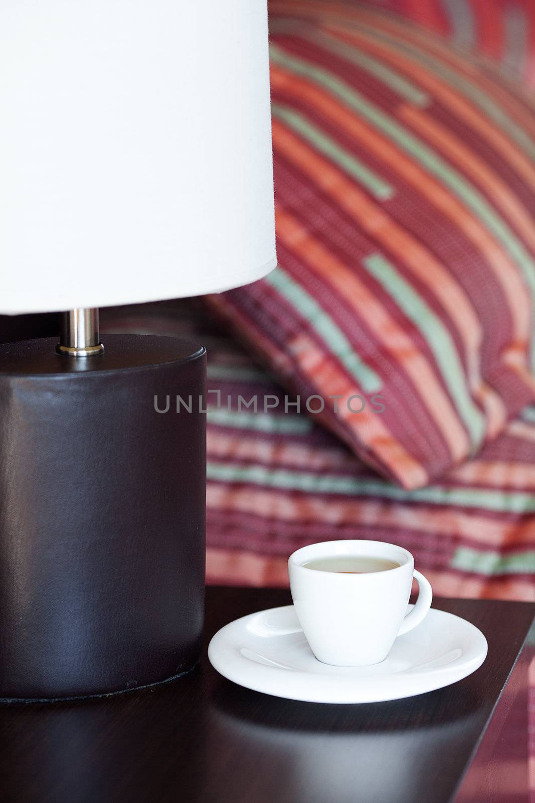 bed with a pillow, a cup of tea on the bedside table and lamp by jannyjus