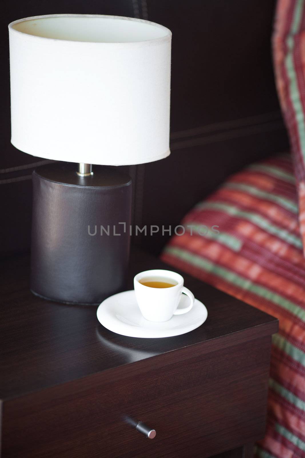 bed with a pillow, a cup of tea on the bedside table and lamp by jannyjus