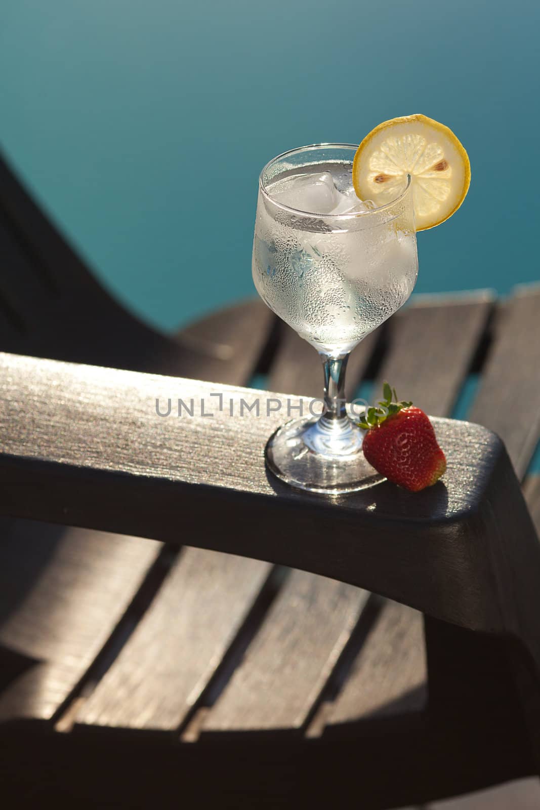 Swimming pool, lounge, a wine glass with ice, lemon and strawberry