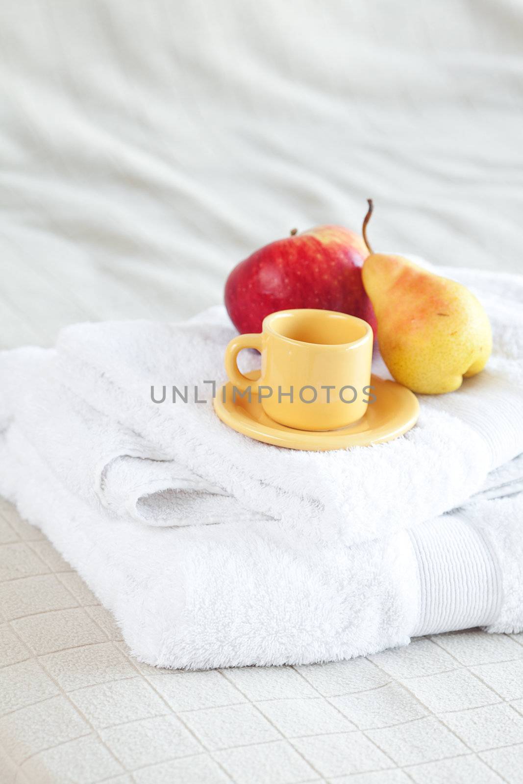 cup,apple and pear on towels on the bed 