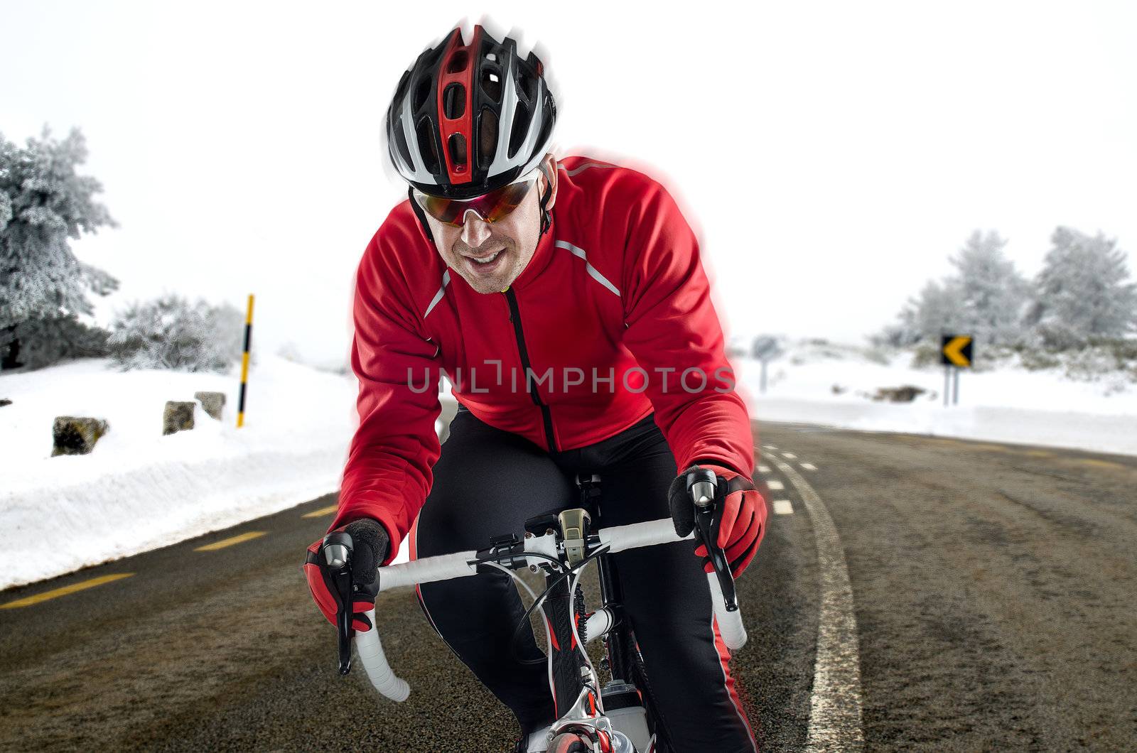 Cyclist on road bike through a asphalt road in the mountains with snow.