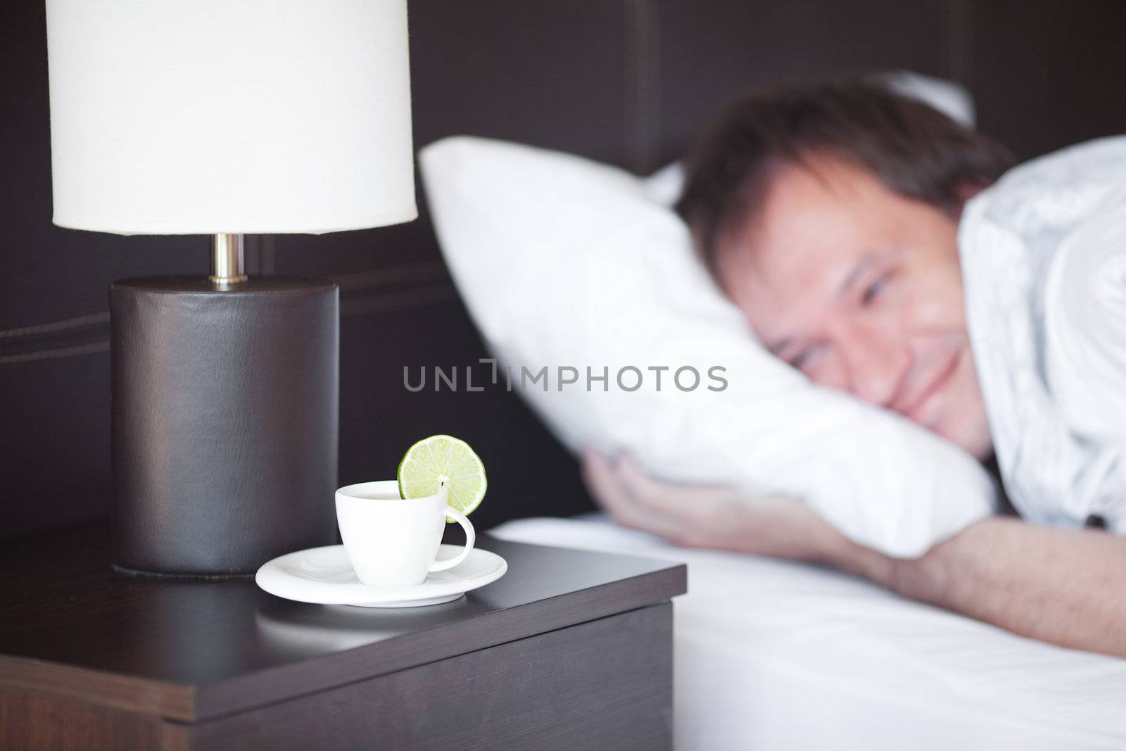 man sleeping on a bed, a cup of tea on the bedside table and lam by jannyjus