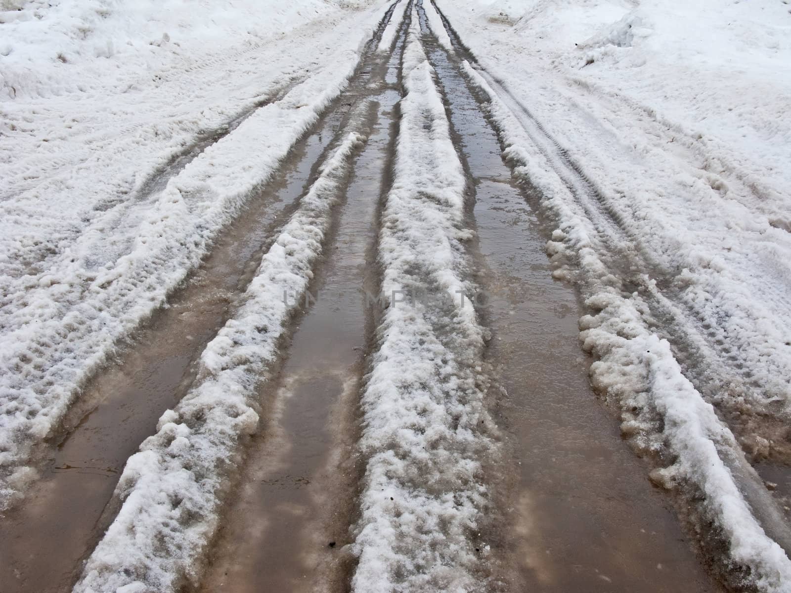 Country road, covered with dirty melting snow puddles in early spring