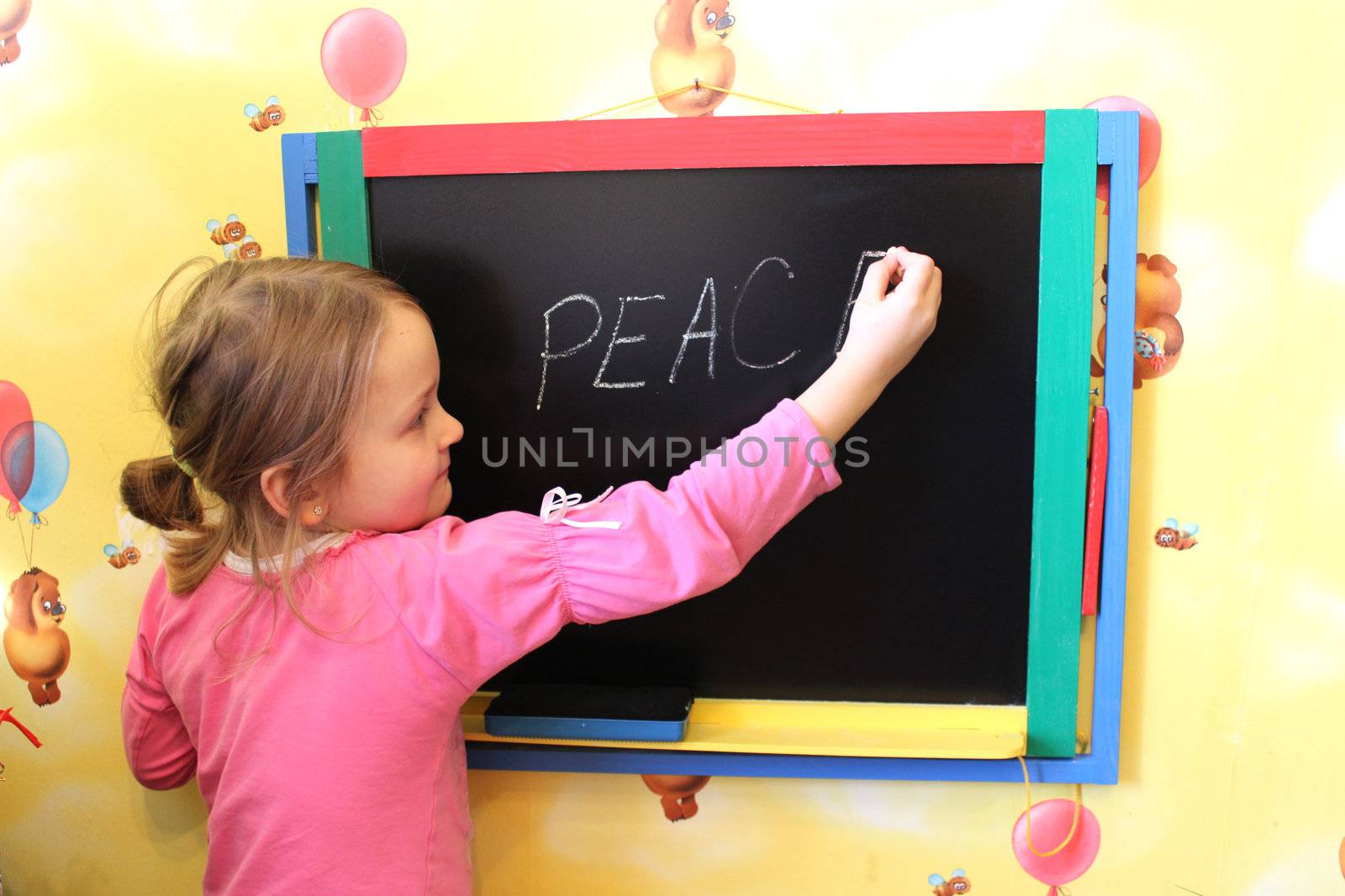 little girl writes on blackboard word Peace